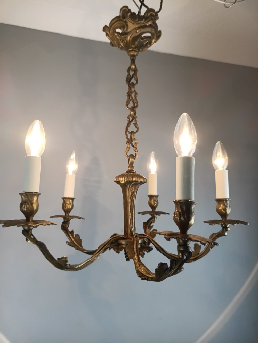 A five-arm dark bronze chandelier with cast acanthus leaf arms, white candle sleeves, and a matching hanging chain with ceiling rose. View XI