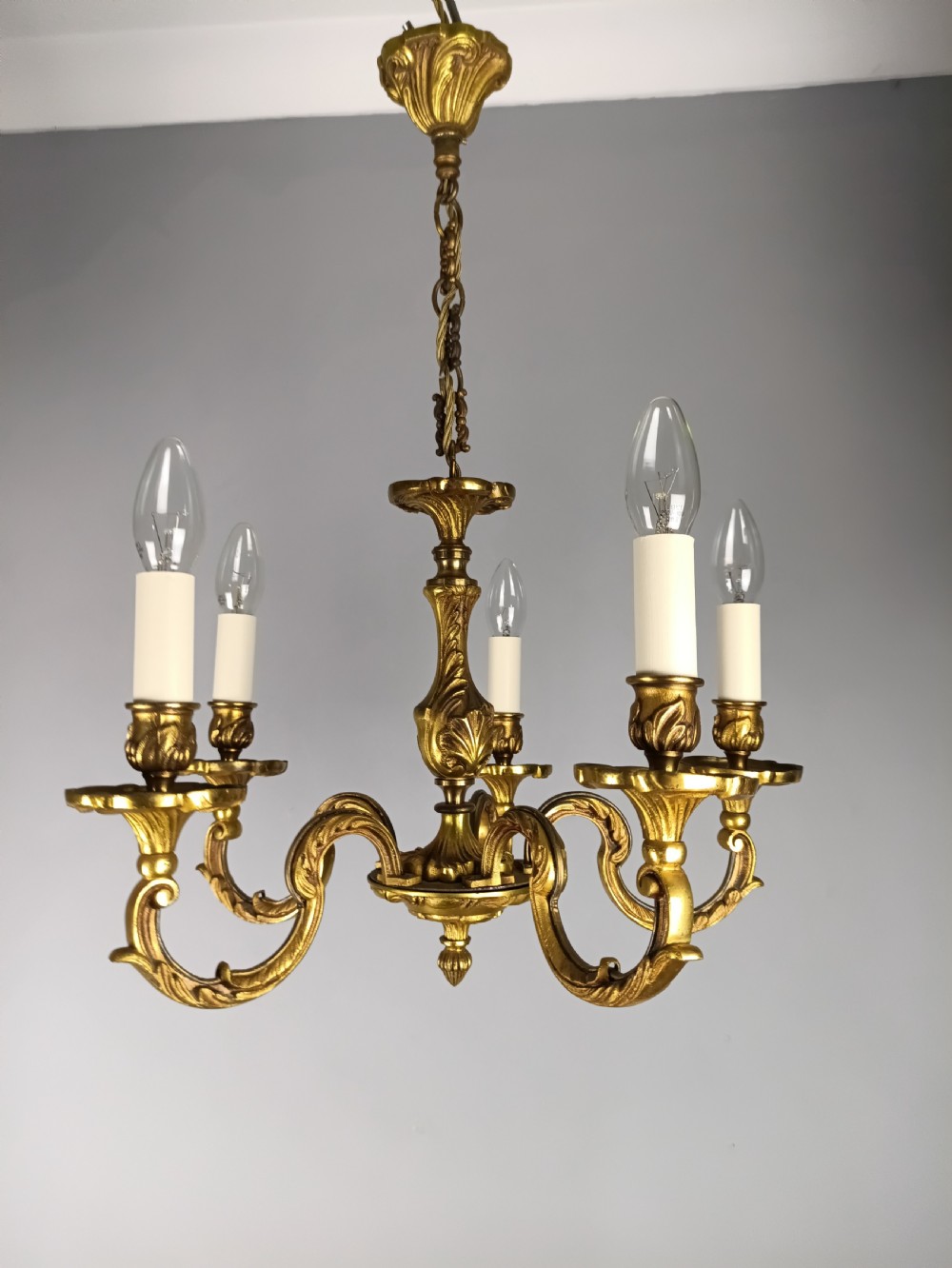 A five-arm French gilt bronze chandelier featuring acanthus leaf scroll arms, candle-style sockets, and an ornate central column suspended by a chain.