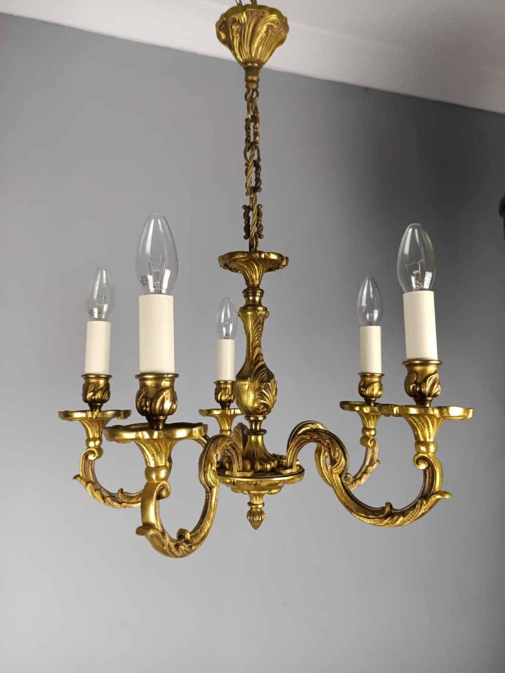 A five-arm French gilt bronze chandelier featuring acanthus leaf scroll arms, candle-style sockets, and an ornate central column suspended by a chain. View VI