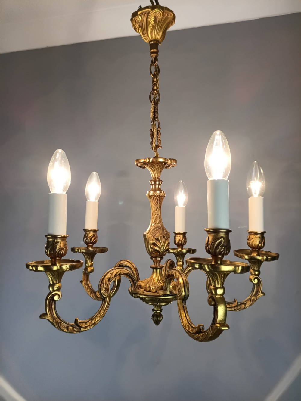 A five-arm French gilt bronze chandelier featuring acanthus leaf scroll arms, candle-style sockets, and an ornate central column suspended by a chain. View X