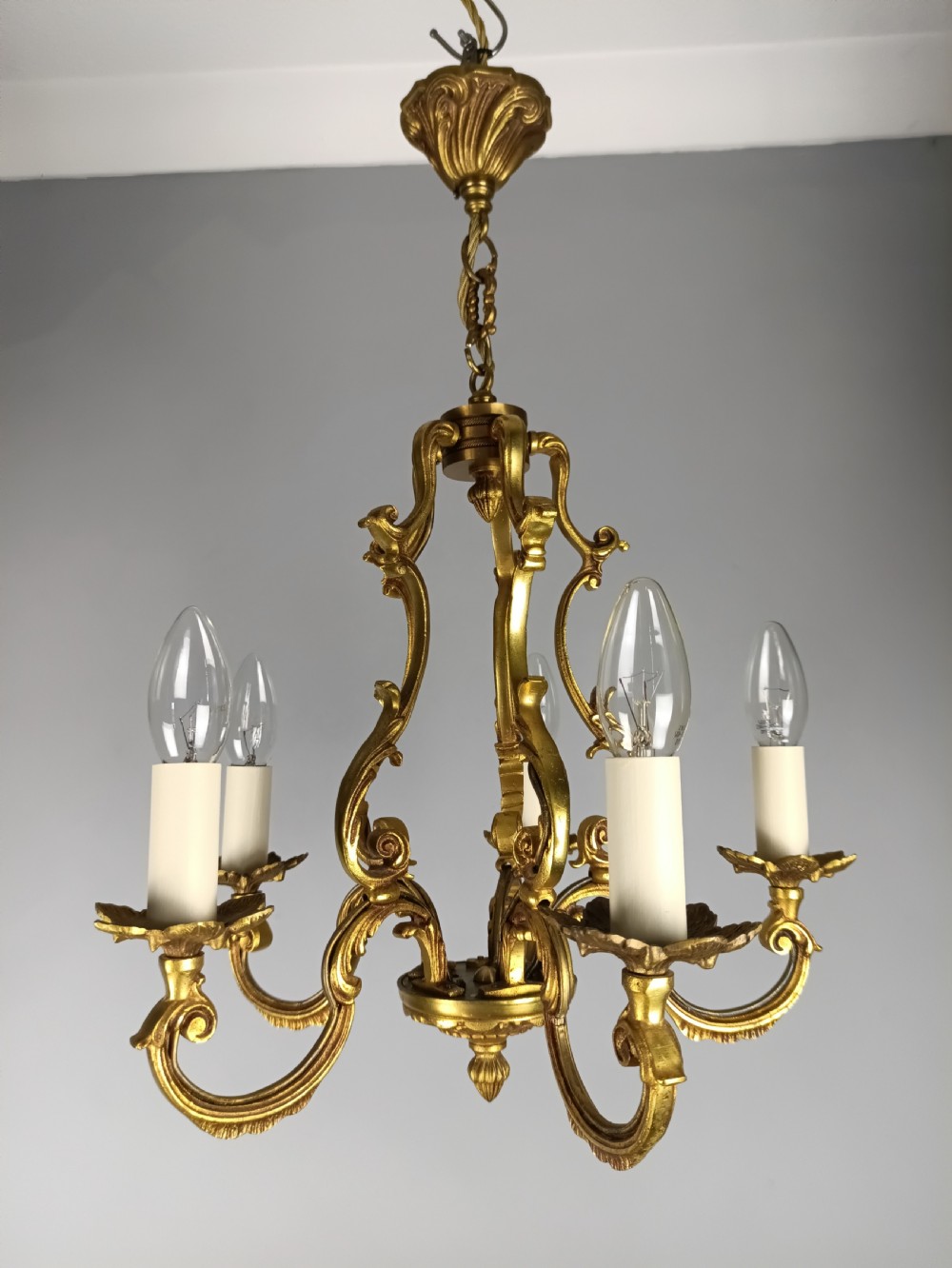 A French five-light gilt bronze birdcage chandelier featuring open rococo scrollwork arms, leafy candle drip pans, and a central open frame suspended by a chain. View II