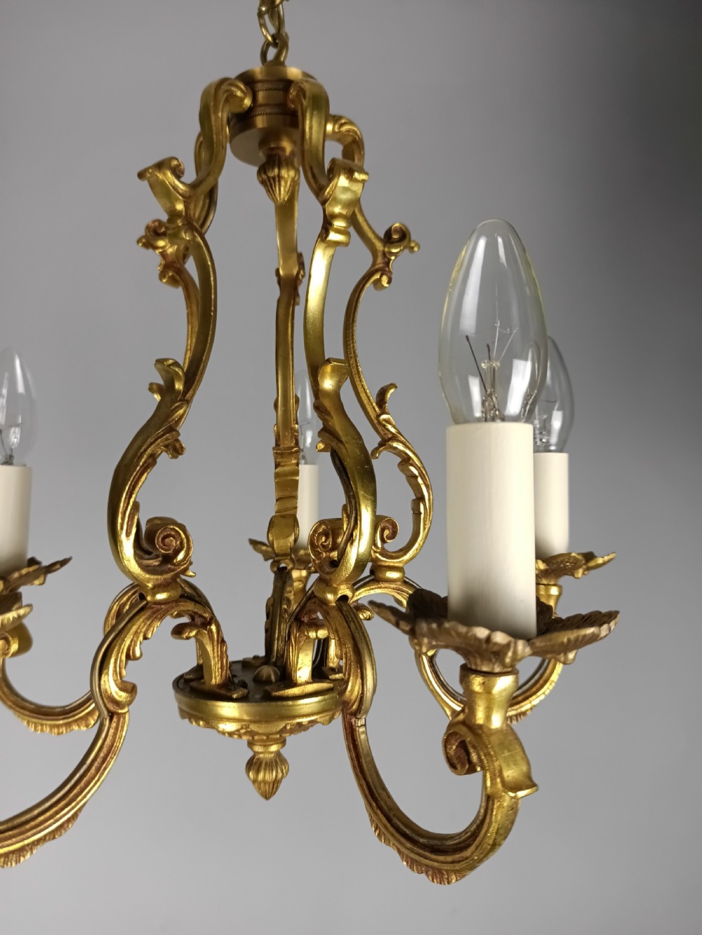 A French five-light gilt bronze birdcage chandelier featuring open rococo scrollwork arms, leafy candle drip pans, and a central open frame suspended by a chain. View V