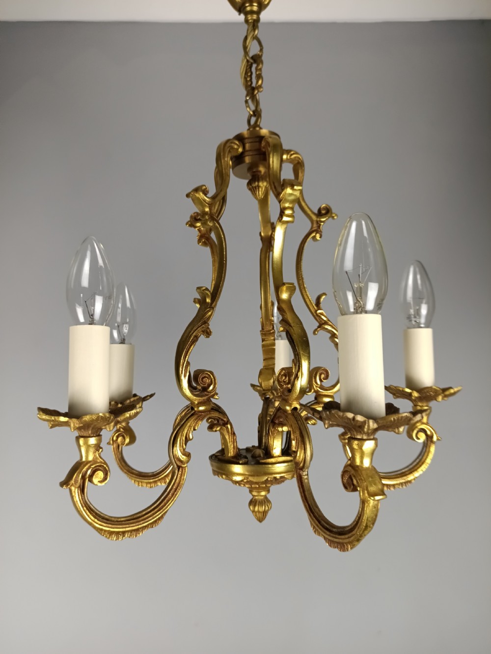 A French five-light gilt bronze birdcage chandelier featuring open rococo scrollwork arms, leafy candle drip pans, and a central open frame suspended by a chain. View VI