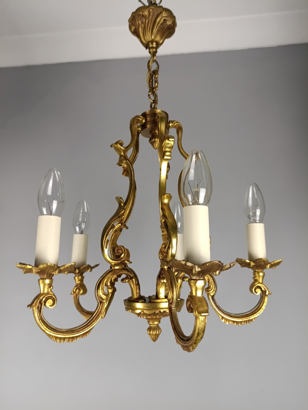 A French five-light gilt bronze birdcage chandelier featuring open rococo scrollwork arms, leafy candle drip pans, and a central open frame suspended by a chain. View VII