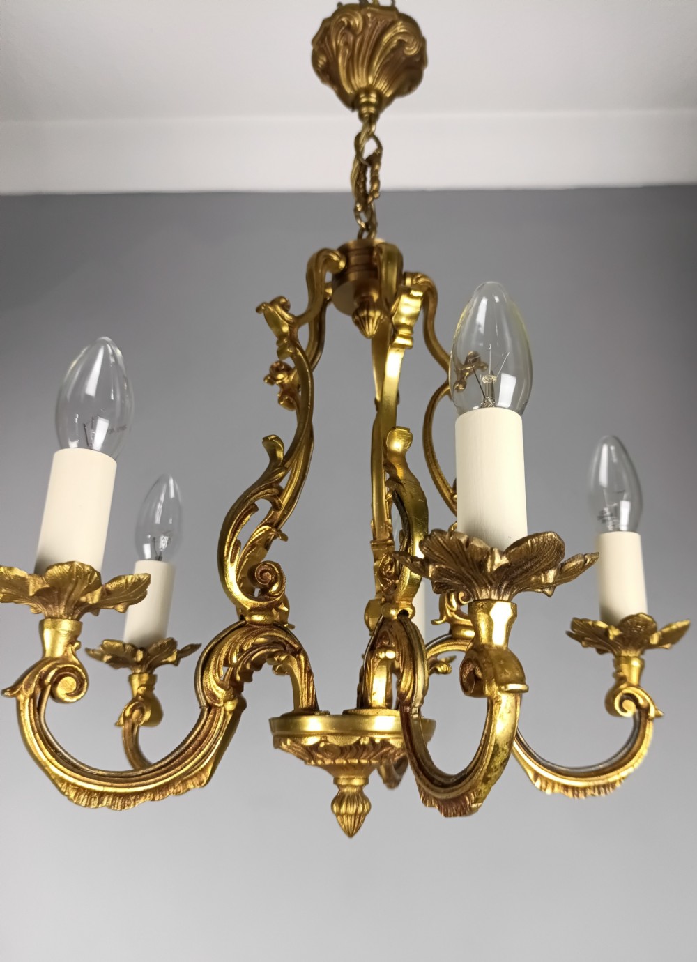 A French five-light gilt bronze birdcage chandelier featuring open rococo scrollwork arms, leafy candle drip pans, and a central open frame suspended by a chain. View VIII