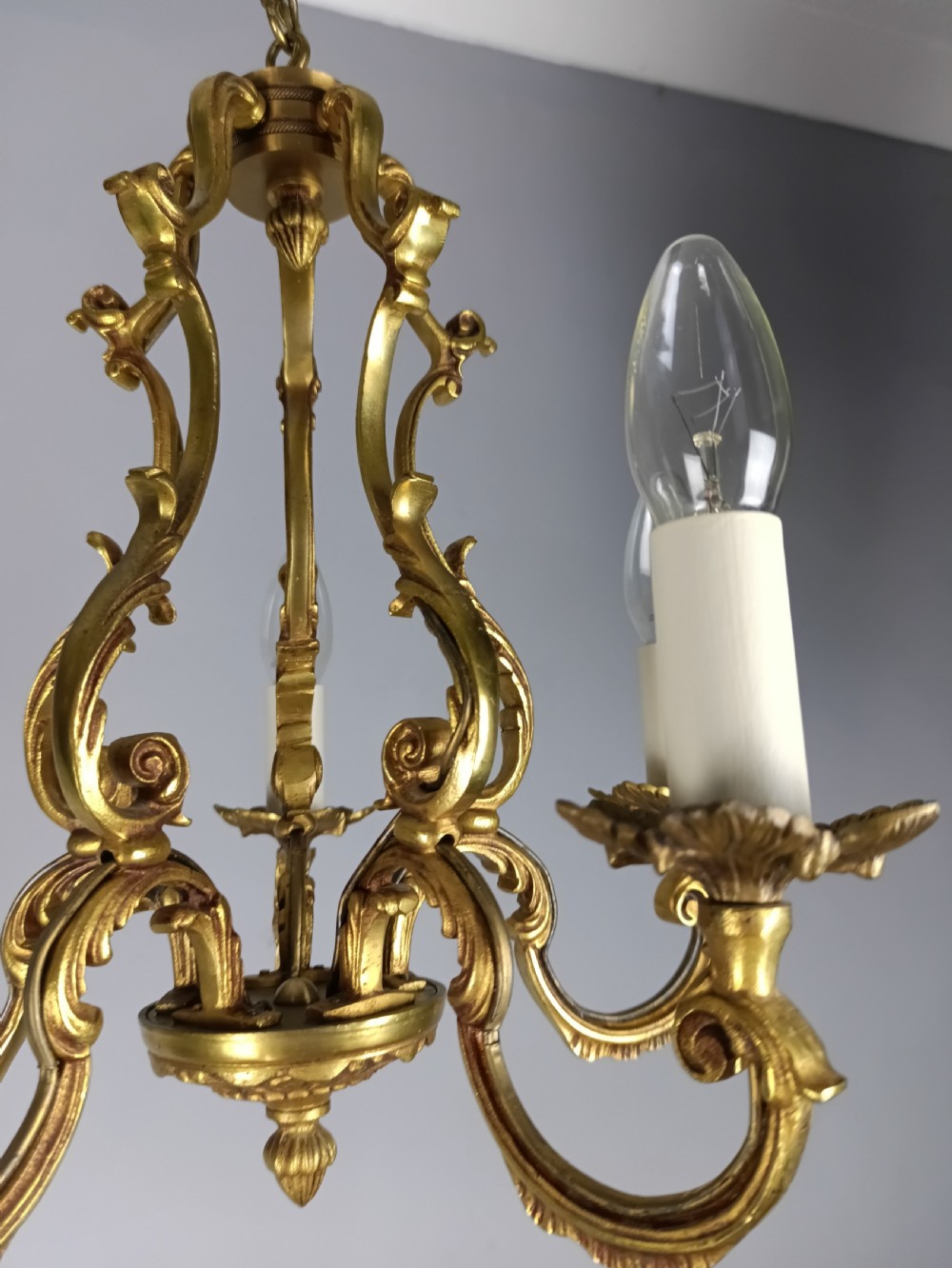 A French five-light gilt bronze birdcage chandelier featuring open rococo scrollwork arms, leafy candle drip pans, and a central open frame suspended by a chain. View IX