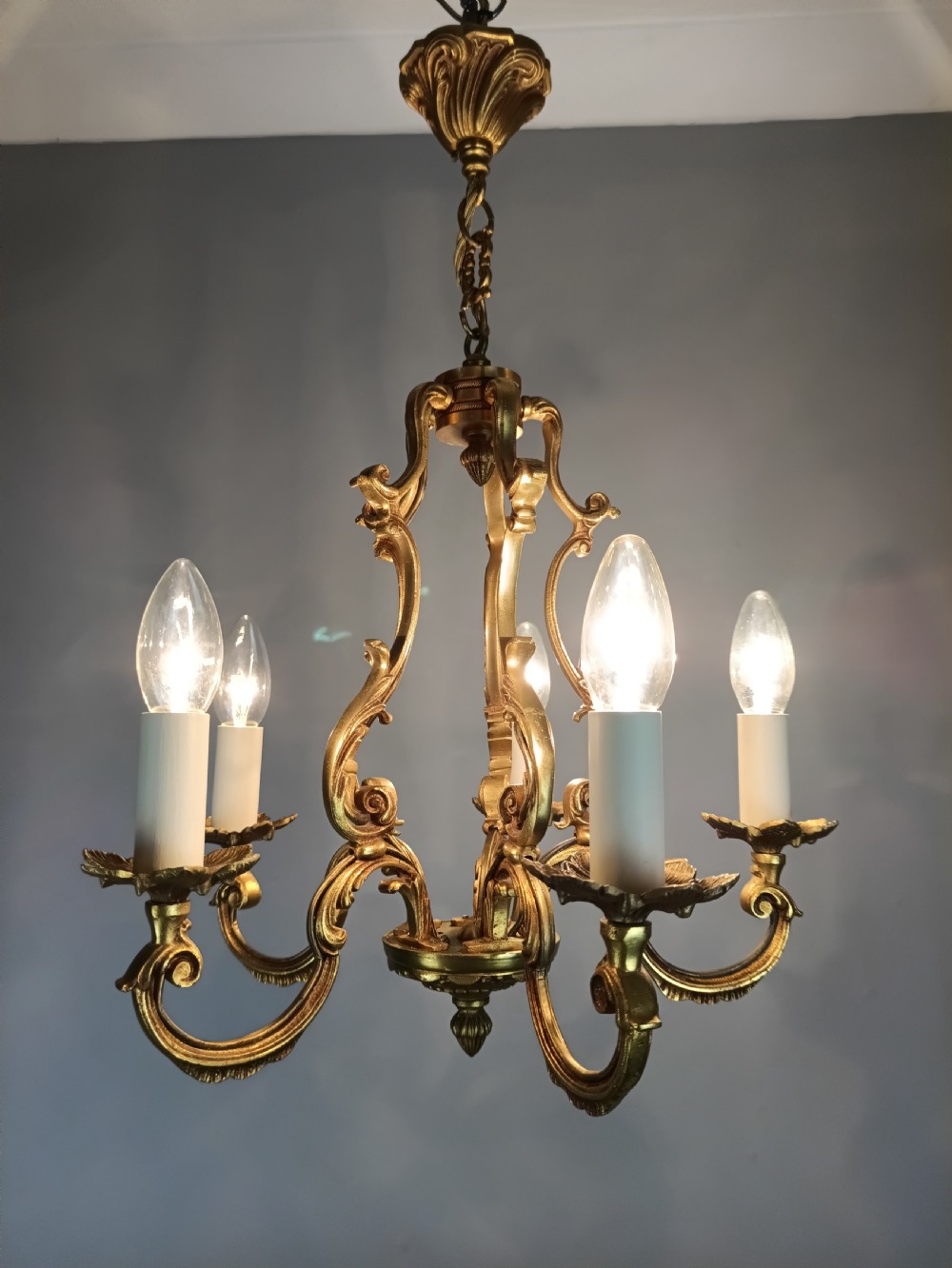 A French five-light gilt bronze birdcage chandelier featuring open rococo scrollwork arms, leafy candle drip pans, and a central open frame suspended by a chain. View X