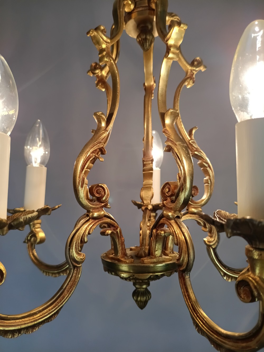 A French five-light gilt bronze birdcage chandelier featuring open rococo scrollwork arms, leafy candle drip pans, and a central open frame suspended by a chain. View XII