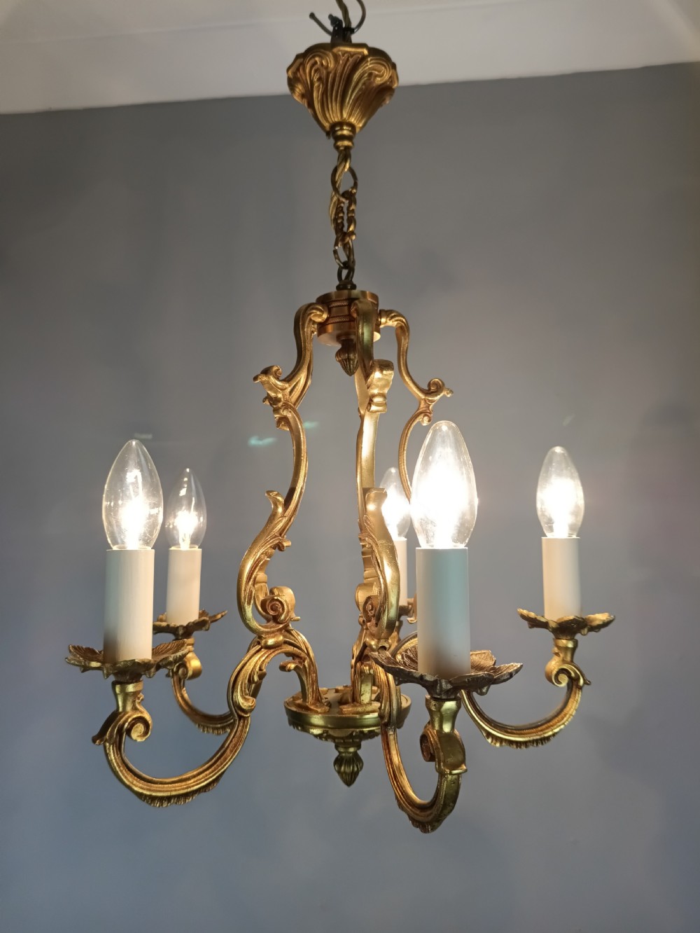 A French five-light gilt bronze birdcage chandelier featuring open rococo scrollwork arms, leafy candle drip pans, and a central open frame suspended by a chain. View XIII