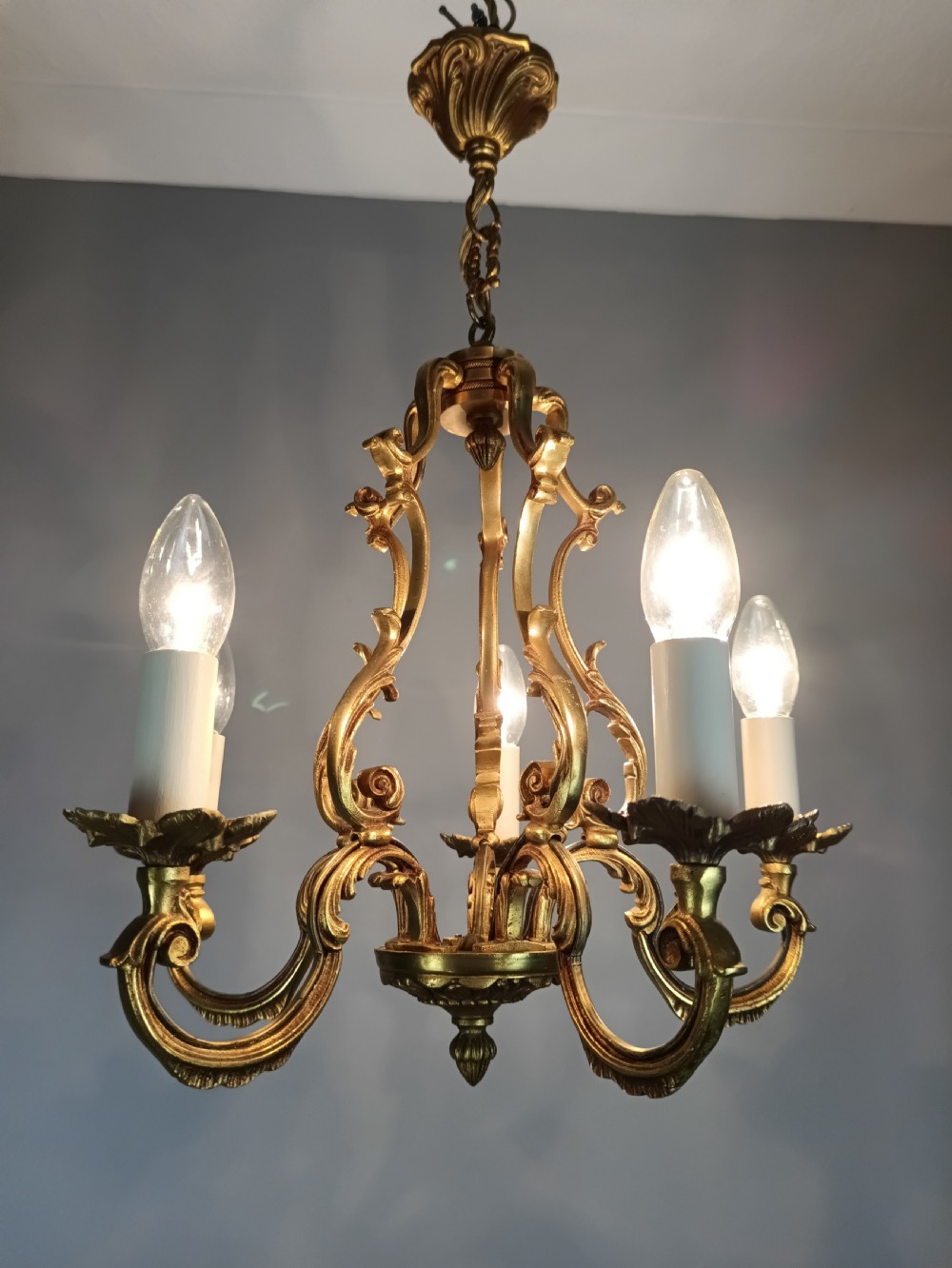A French five-light gilt bronze birdcage chandelier featuring open rococo scrollwork arms, leafy candle drip pans, and a central open frame suspended by a chain. View XIV
