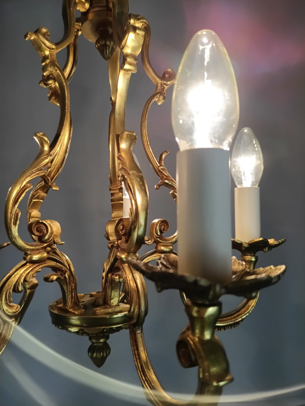 A French five-light gilt bronze birdcage chandelier featuring open rococo scrollwork arms, leafy candle drip pans, and a central open frame suspended by a chain. View XV