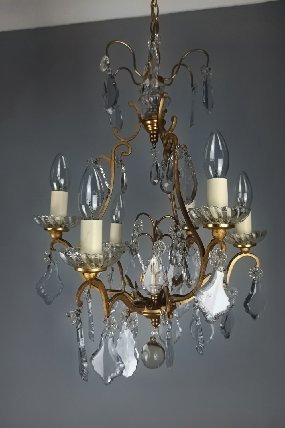 A French six-light birdcage chandelier featuring a gilded scroll frame decorated with clear faceted crystal drops and glass candle drip pans.