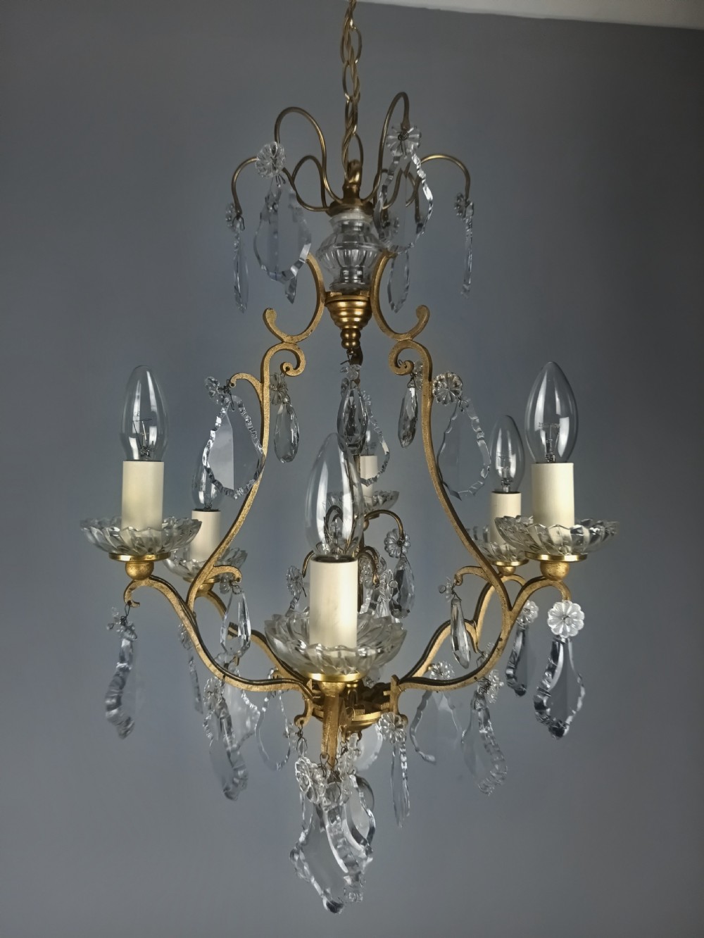 A French six-light birdcage chandelier featuring a gilded scroll frame decorated with clear faceted crystal drops and glass candle drip pans. View VI