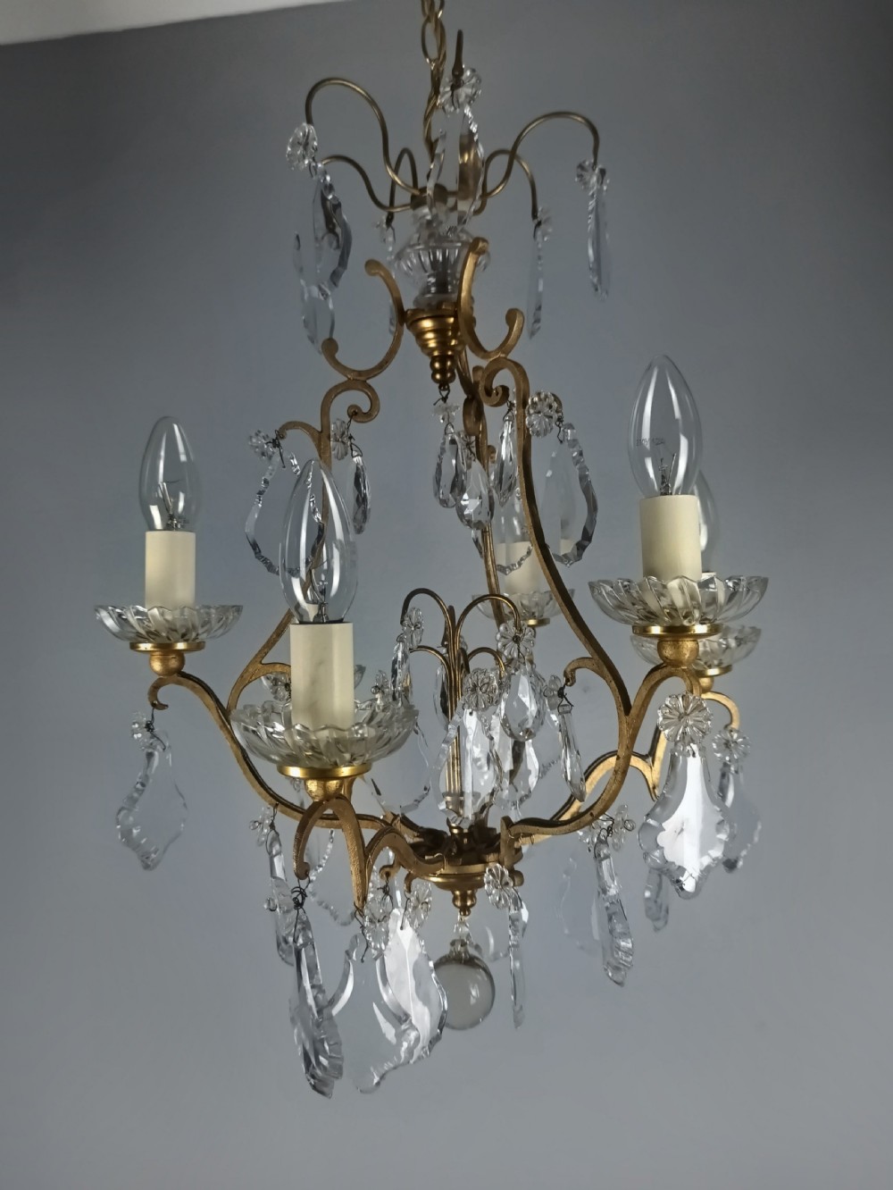 A French six-light birdcage chandelier featuring a gilded scroll frame decorated with clear faceted crystal drops and glass candle drip pans. View X