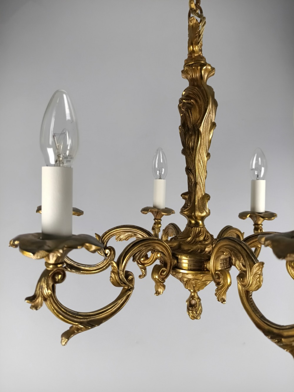 A French six-light gilt bronze chandelier featuring scrolling acanthus leaf arms, candle-style bulb sleeves, and an ornamental central stem suspended from a chain. View III