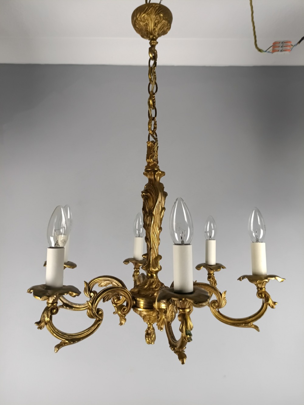 A French six-light gilt bronze chandelier featuring scrolling acanthus leaf arms, candle-style bulb sleeves, and an ornamental central stem suspended from a chain. View VIII