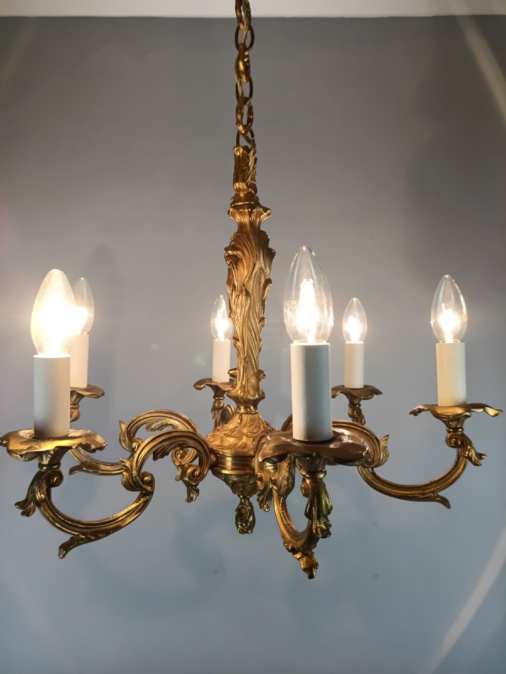 A French six-light gilt bronze chandelier featuring scrolling acanthus leaf arms, candle-style bulb sleeves, and an ornamental central stem suspended from a chain. View IX