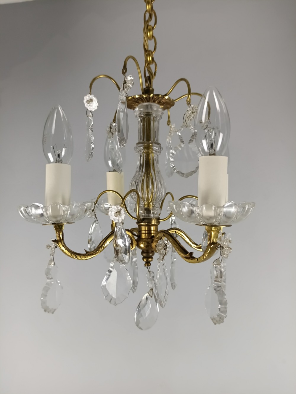 A four-arm brass mini chandelier featuring clear glass droplets, floral bobeches, and a central glass stem column. View II