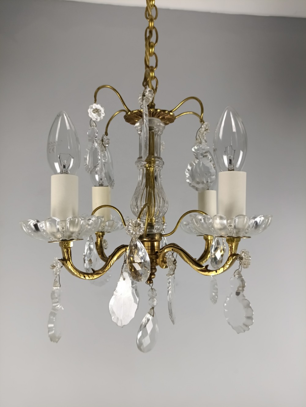 A four-arm brass mini chandelier featuring clear glass droplets, floral bobeches, and a central glass stem column. View III