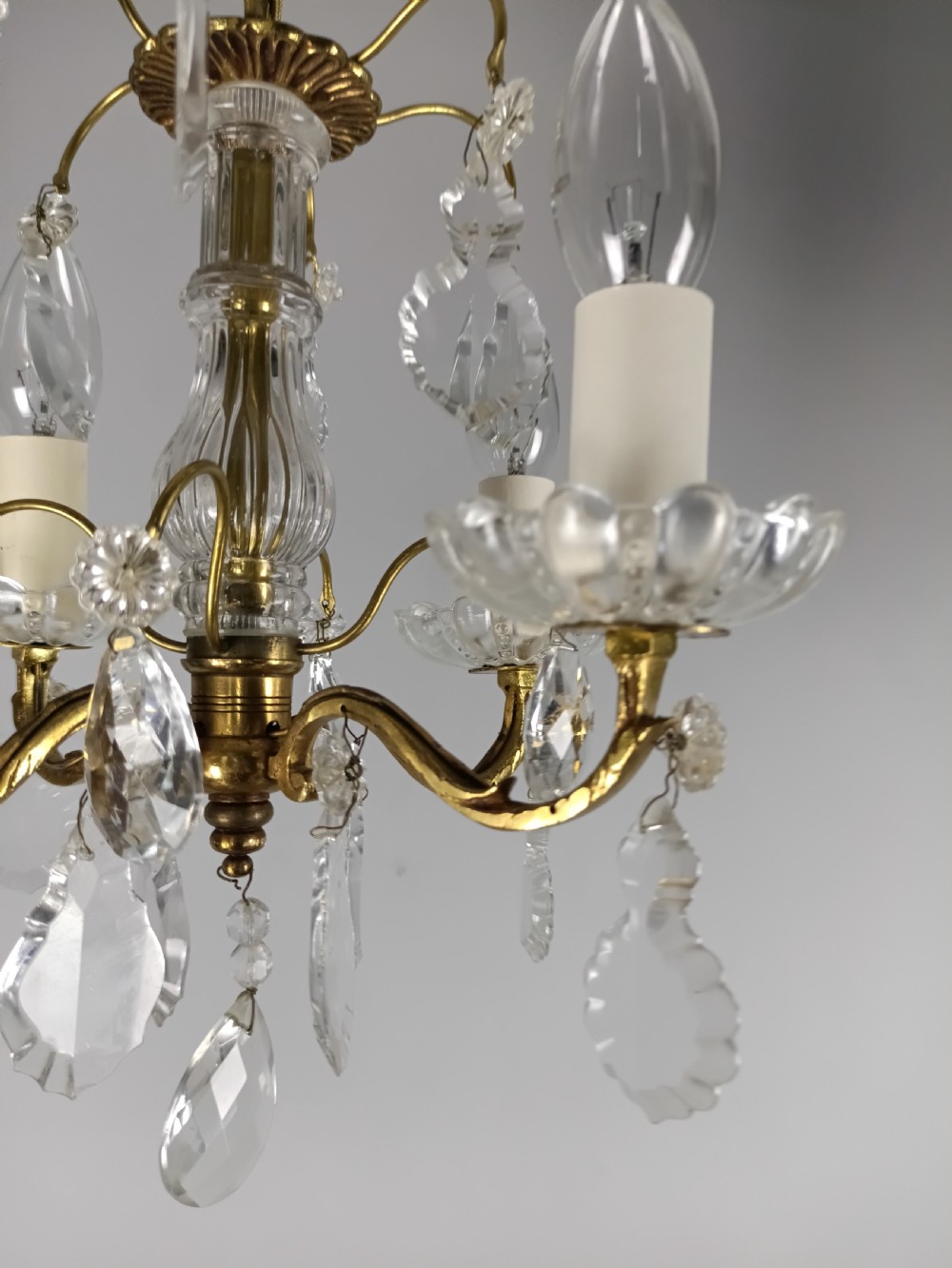 A four-arm brass mini chandelier featuring clear glass droplets, floral bobeches, and a central glass stem column. View IV