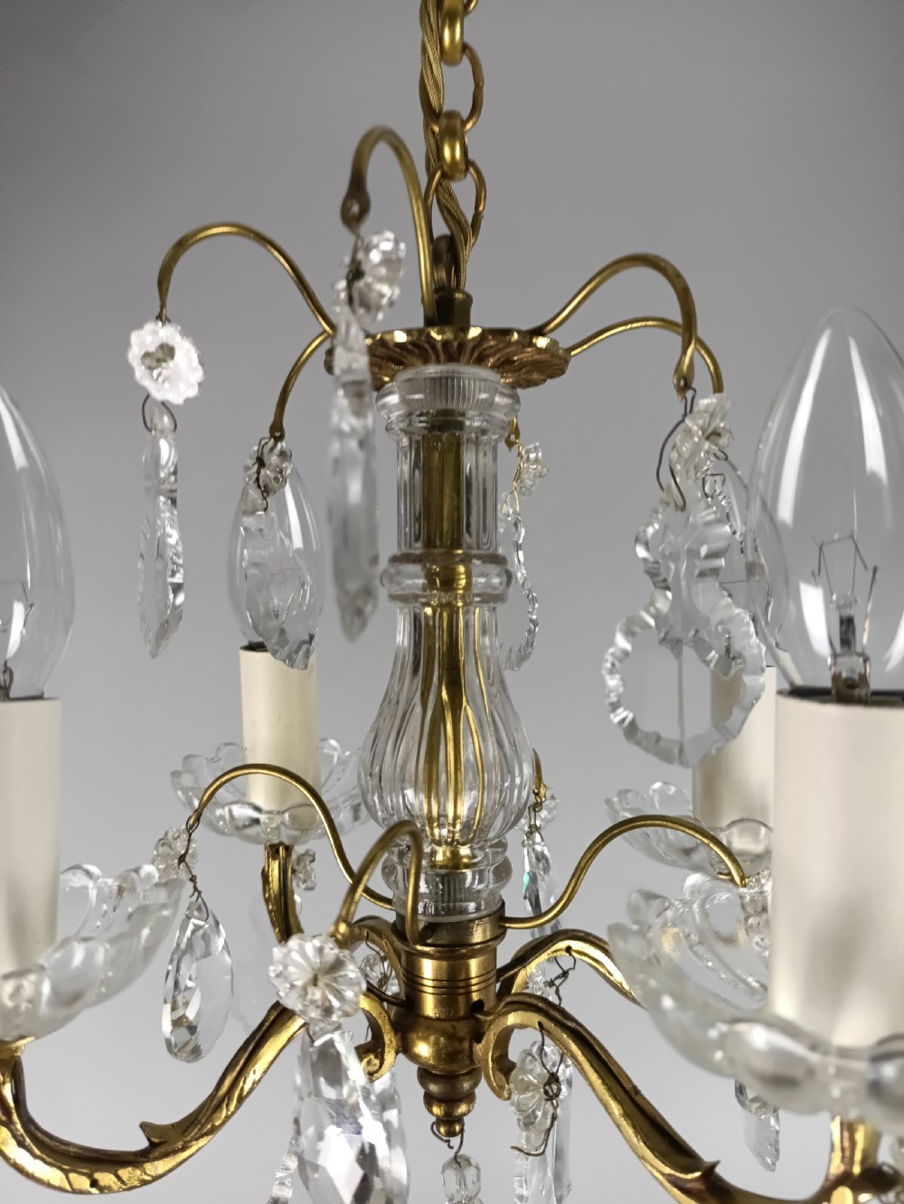 A four-arm brass mini chandelier featuring clear glass droplets, floral bobeches, and a central glass stem column. View V