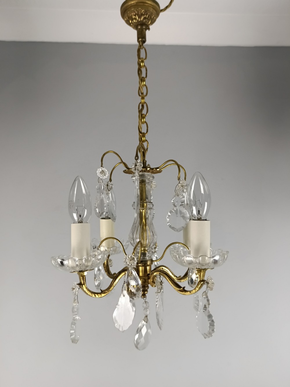 A four-arm brass mini chandelier featuring clear glass droplets, floral bobeches, and a central glass stem column. View VII