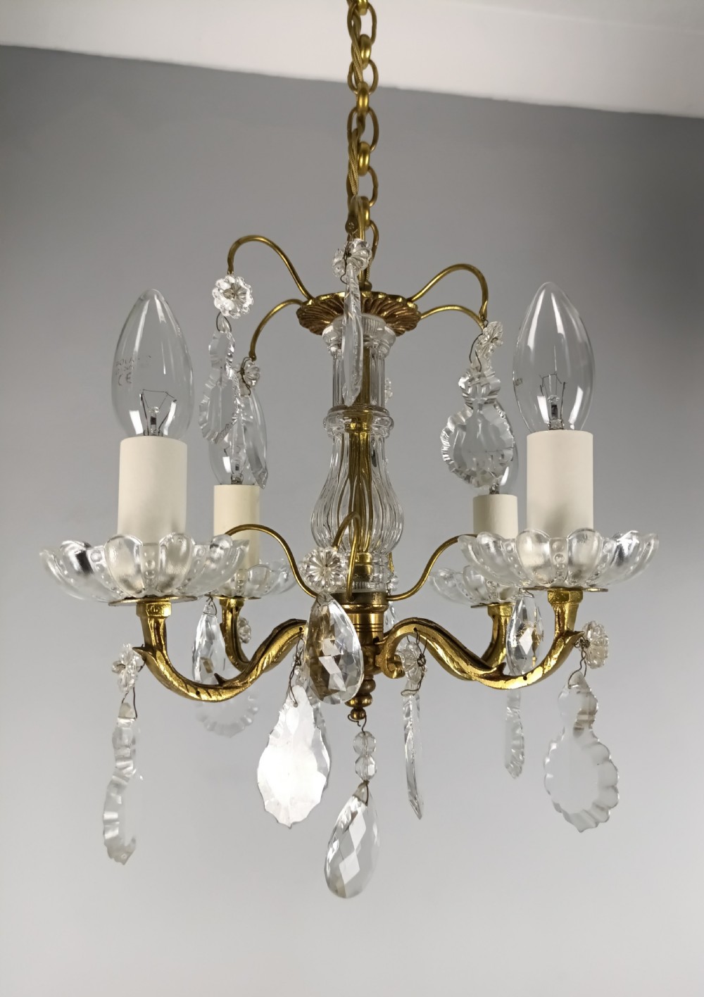 A four-arm brass mini chandelier featuring clear glass droplets, floral bobeches, and a central glass stem column. View VIII
