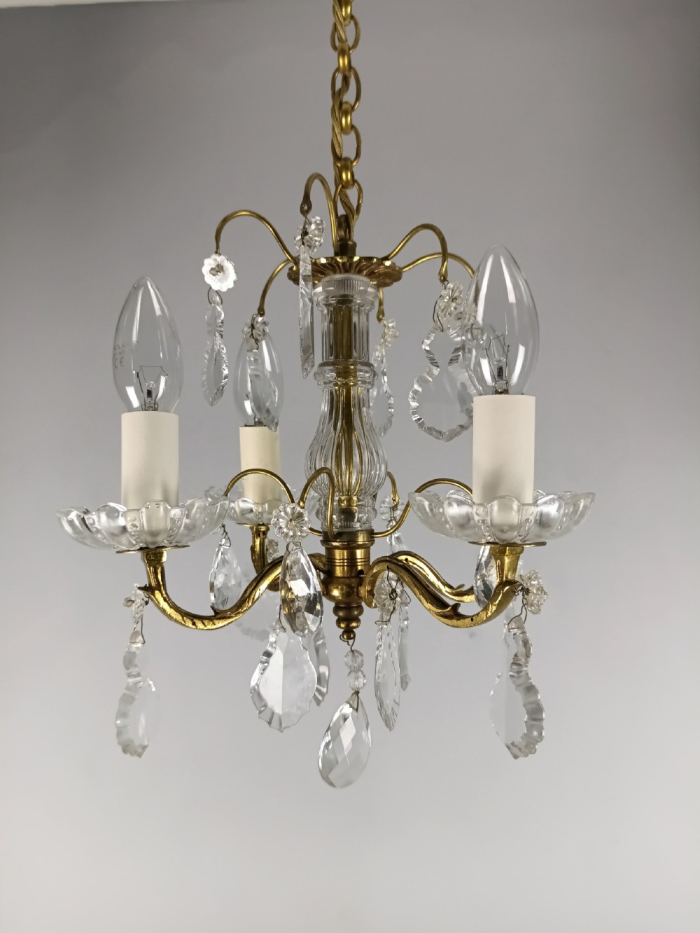 A four-arm brass mini chandelier featuring clear glass droplets, floral bobeches, and a central glass stem column. View IX