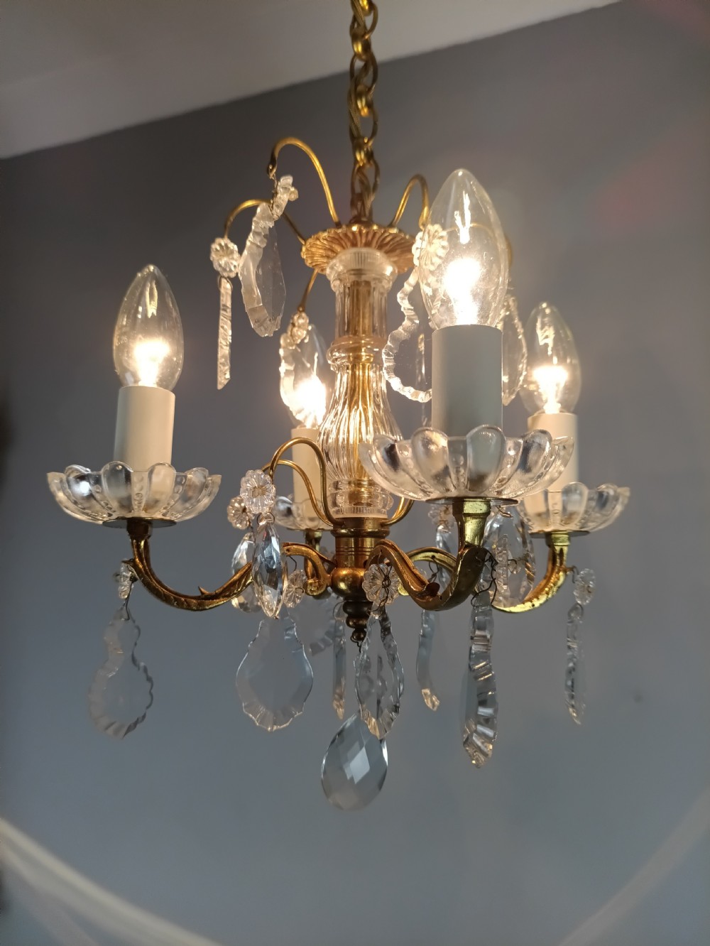 A four-arm brass mini chandelier featuring clear glass droplets, floral bobeches, and a central glass stem column. View XI