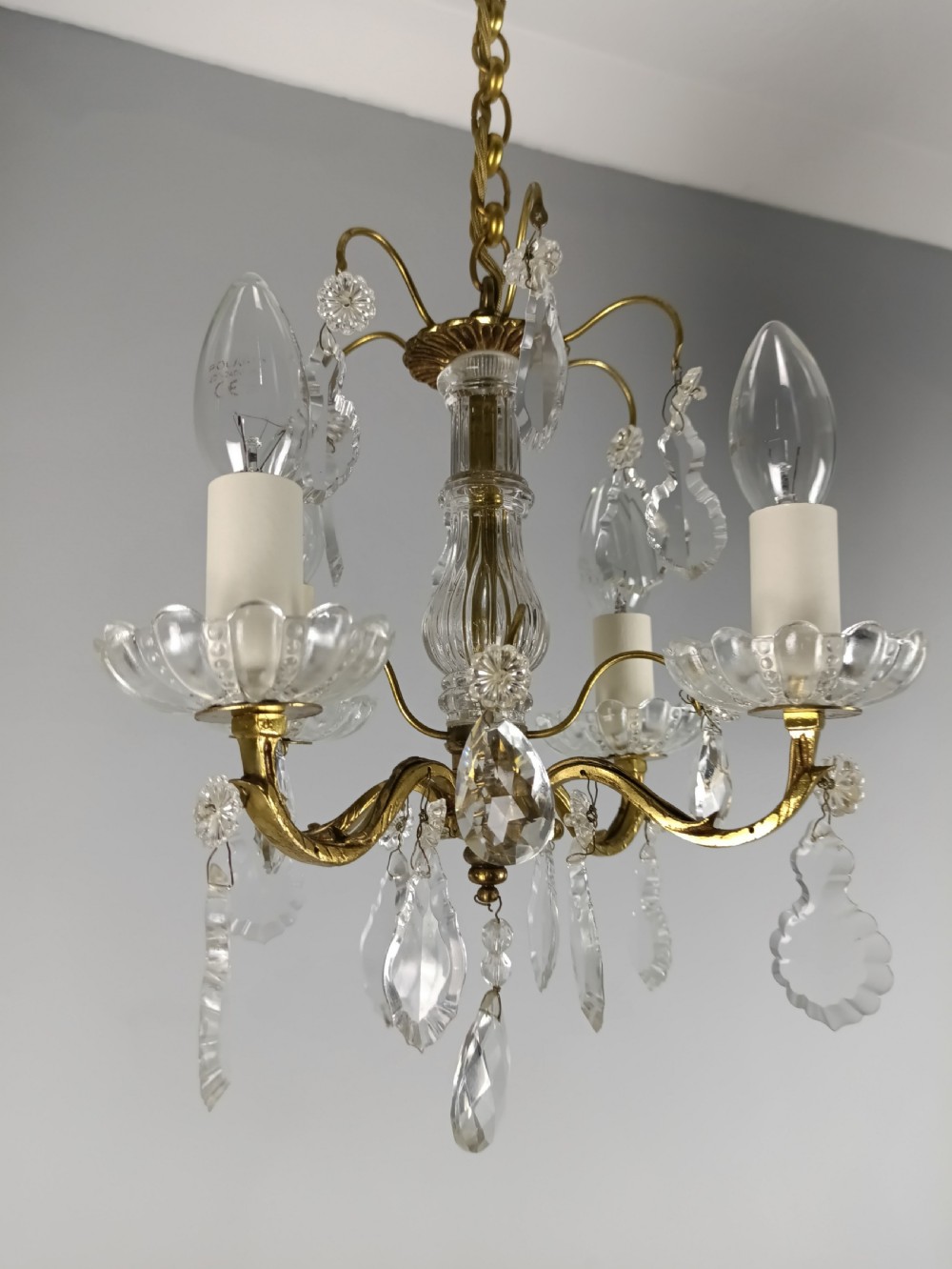 A four-arm brass mini chandelier featuring clear glass droplets, floral bobeches, and a central glass stem column. View XII