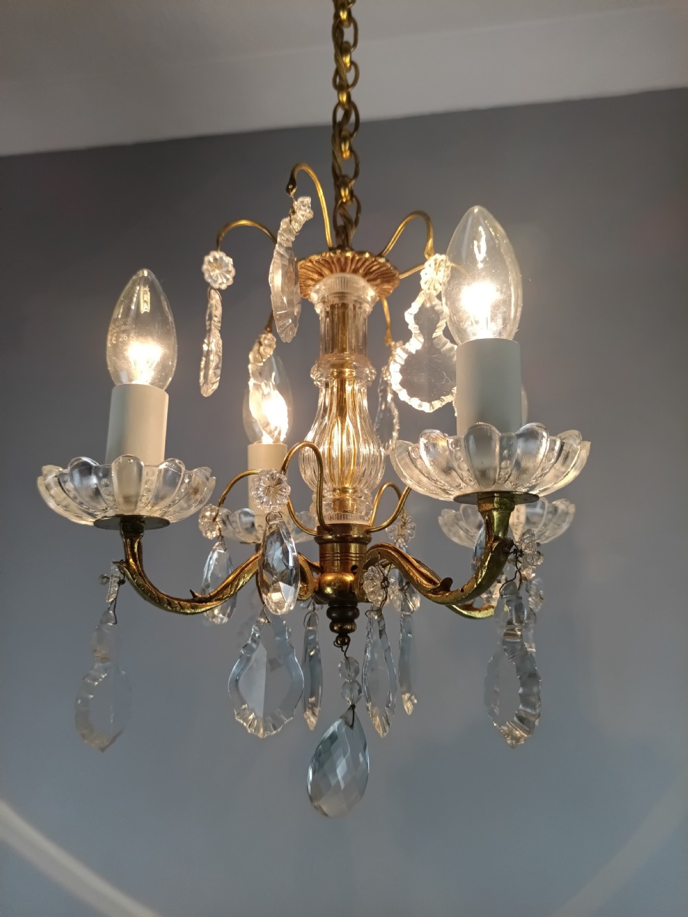 A four-arm brass mini chandelier featuring clear glass droplets, floral bobeches, and a central glass stem column. View XIII