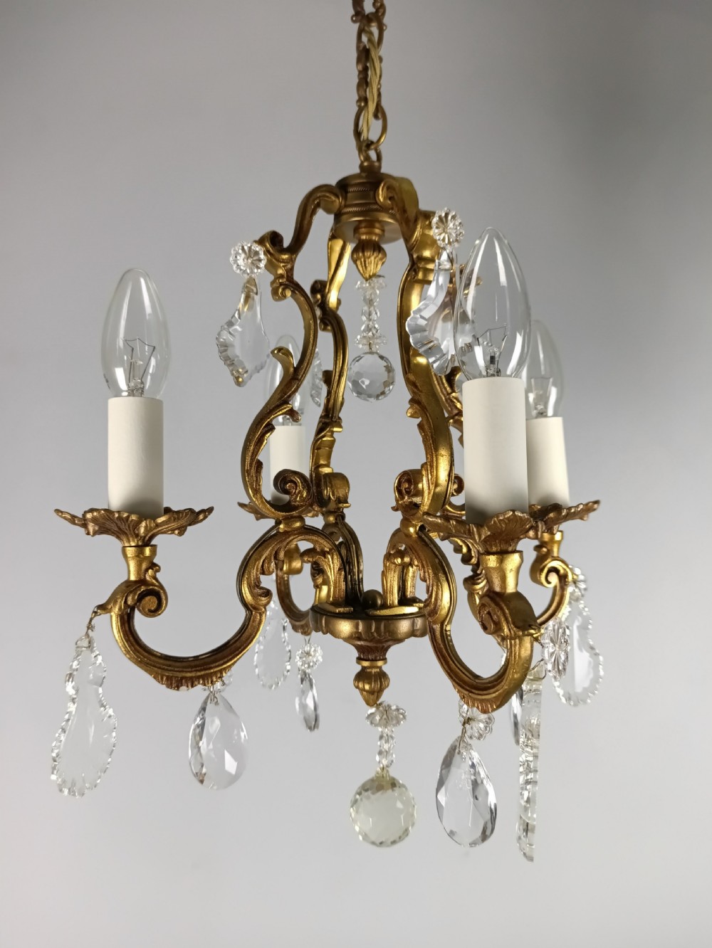 A four-arm French gilt metal chandelier decorated with scrolling arms, candle-style light sockets, and hanging faceted cut crystal drops. View IX