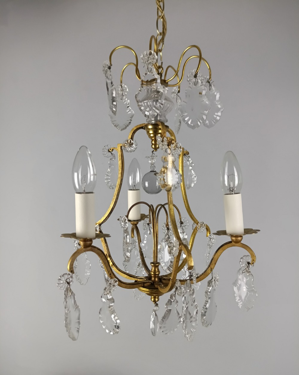 A French gilded metal three-arm birdcage chandelier with hanging clear crystal droplets and glass rosette accents.