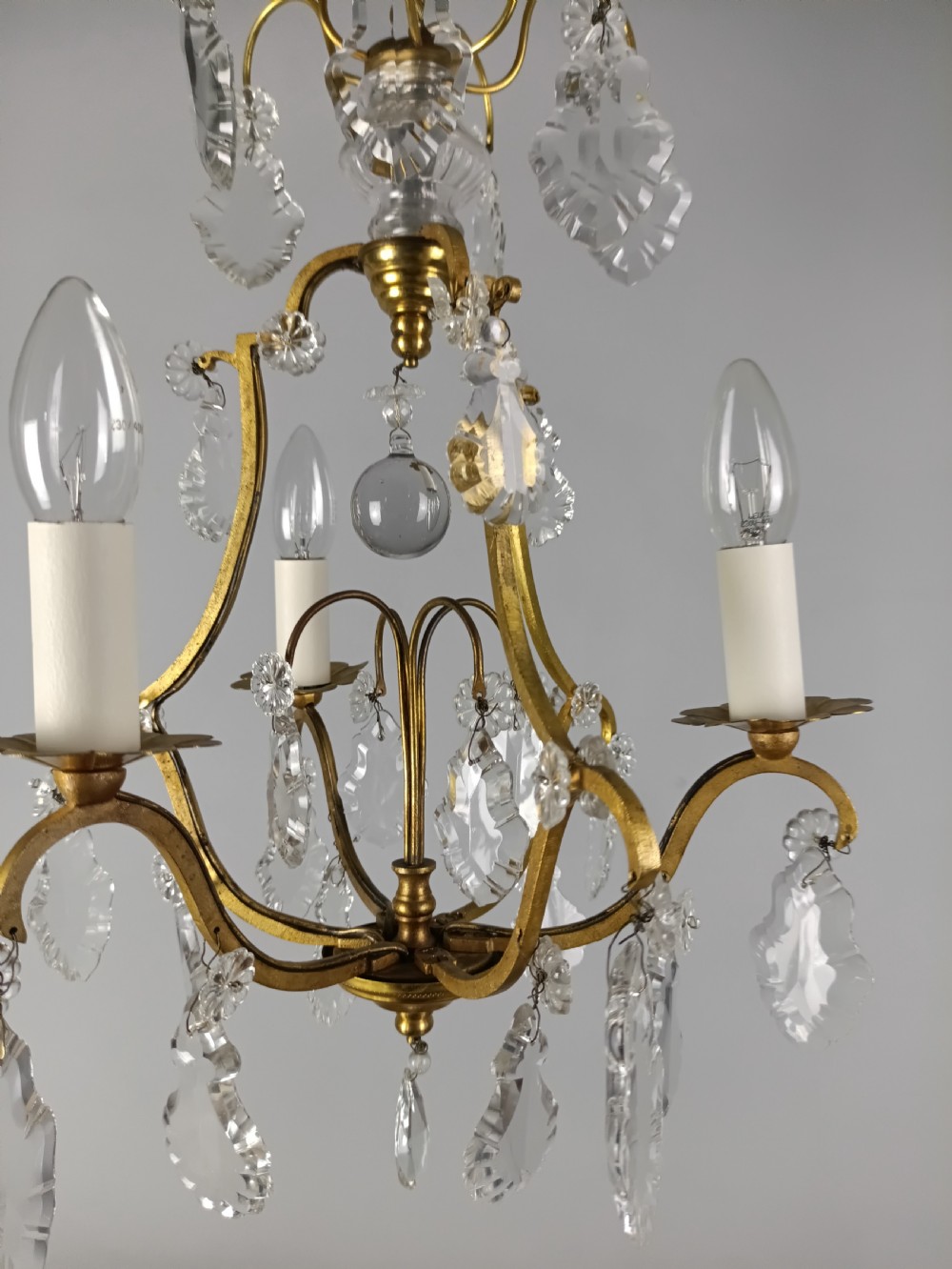 A French gilded metal three-arm birdcage chandelier with hanging clear crystal droplets and glass rosette accents. View II