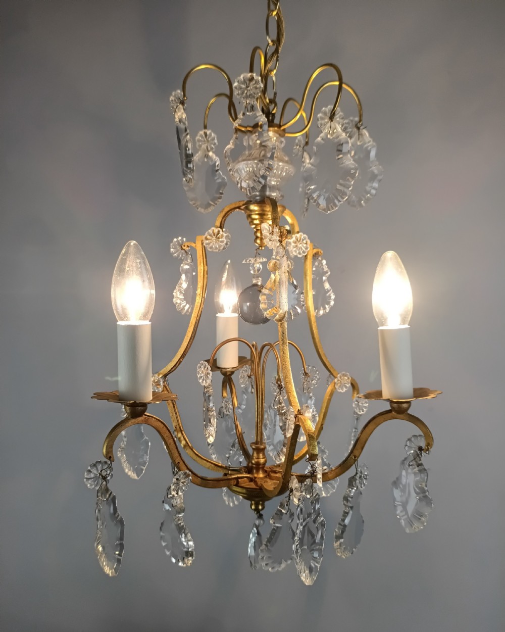 A French gilded metal three-arm birdcage chandelier with hanging clear crystal droplets and glass rosette accents. View X