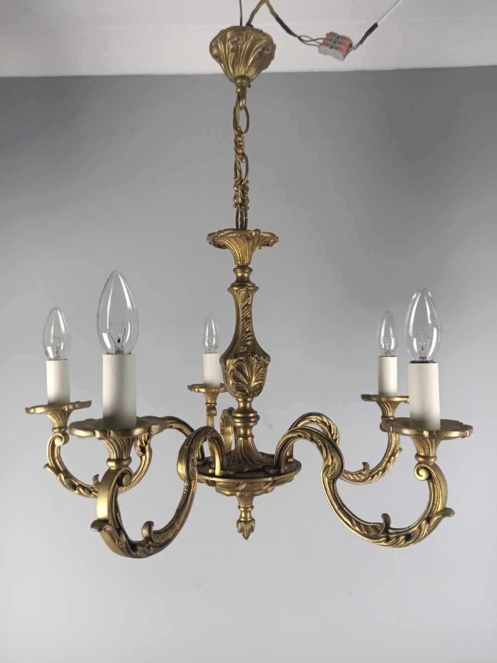 A French gilt brass five-arm chandelier featuring ornate scrolled branches, leaf motifs, and candle bulb sockets suspended from a central chain.