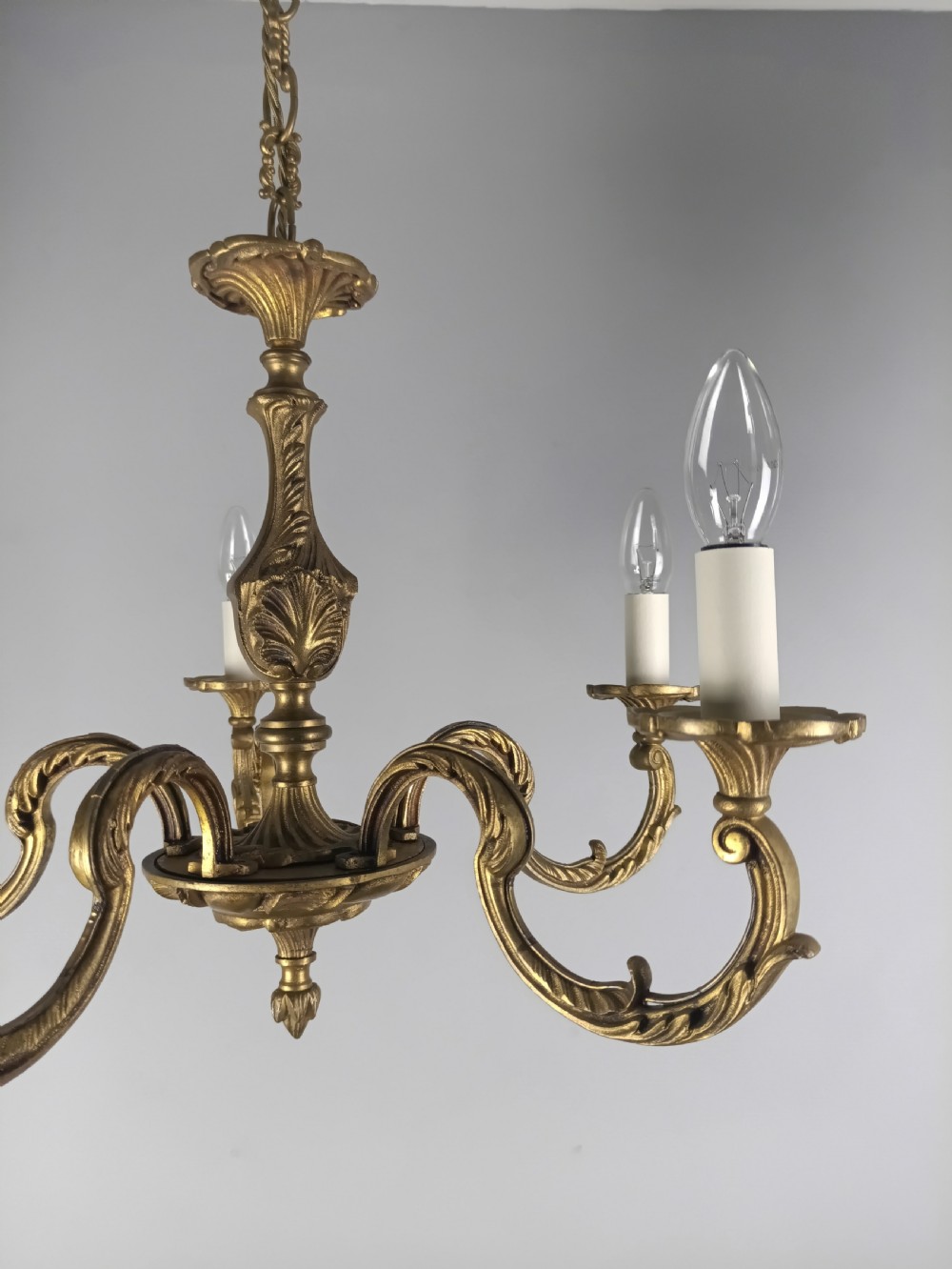 A French gilt brass five-arm chandelier featuring ornate scrolled branches, leaf motifs, and candle bulb sockets suspended from a central chain. View II