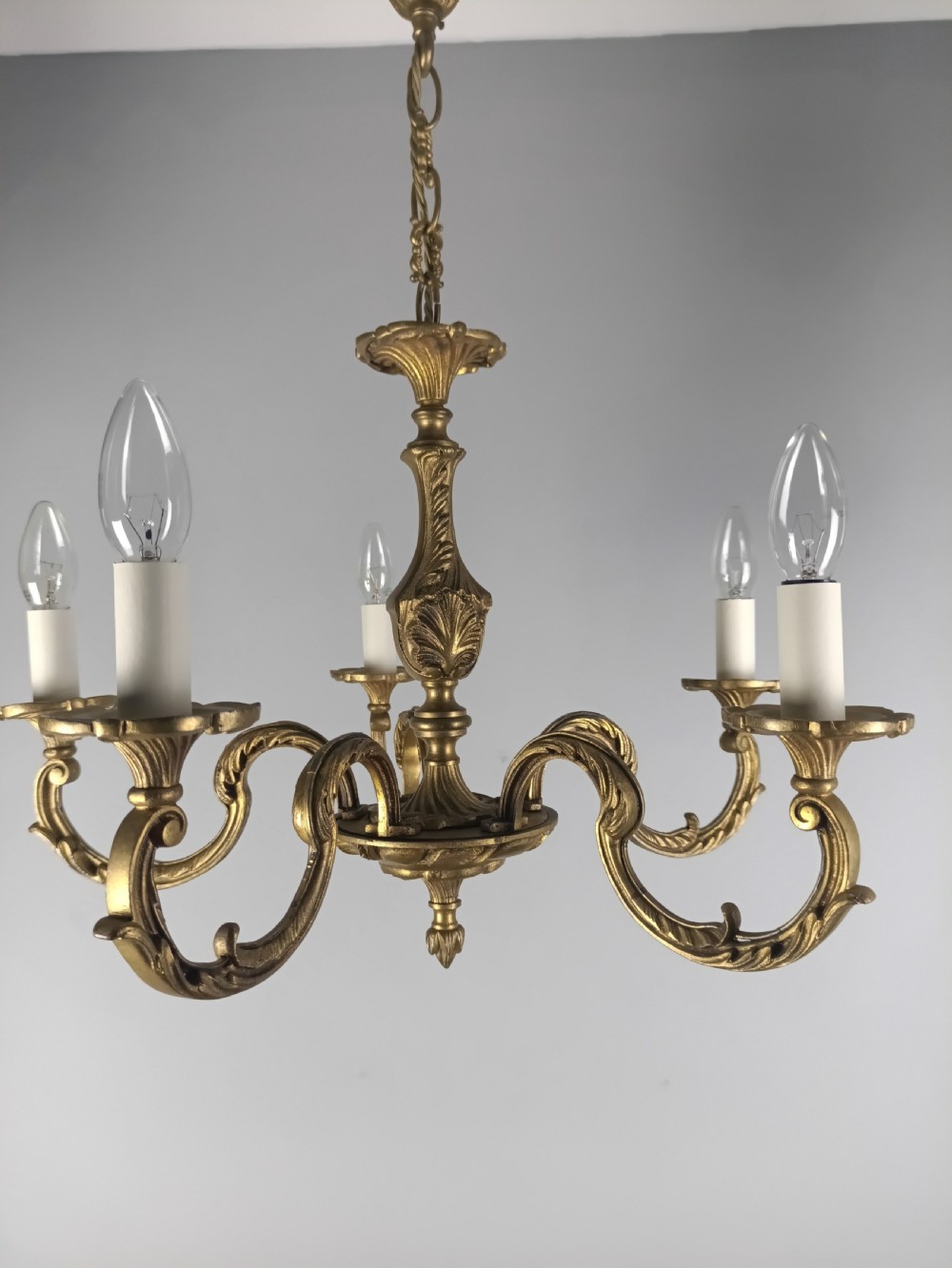 A French gilt brass five-arm chandelier featuring ornate scrolled branches, leaf motifs, and candle bulb sockets suspended from a central chain. View III
