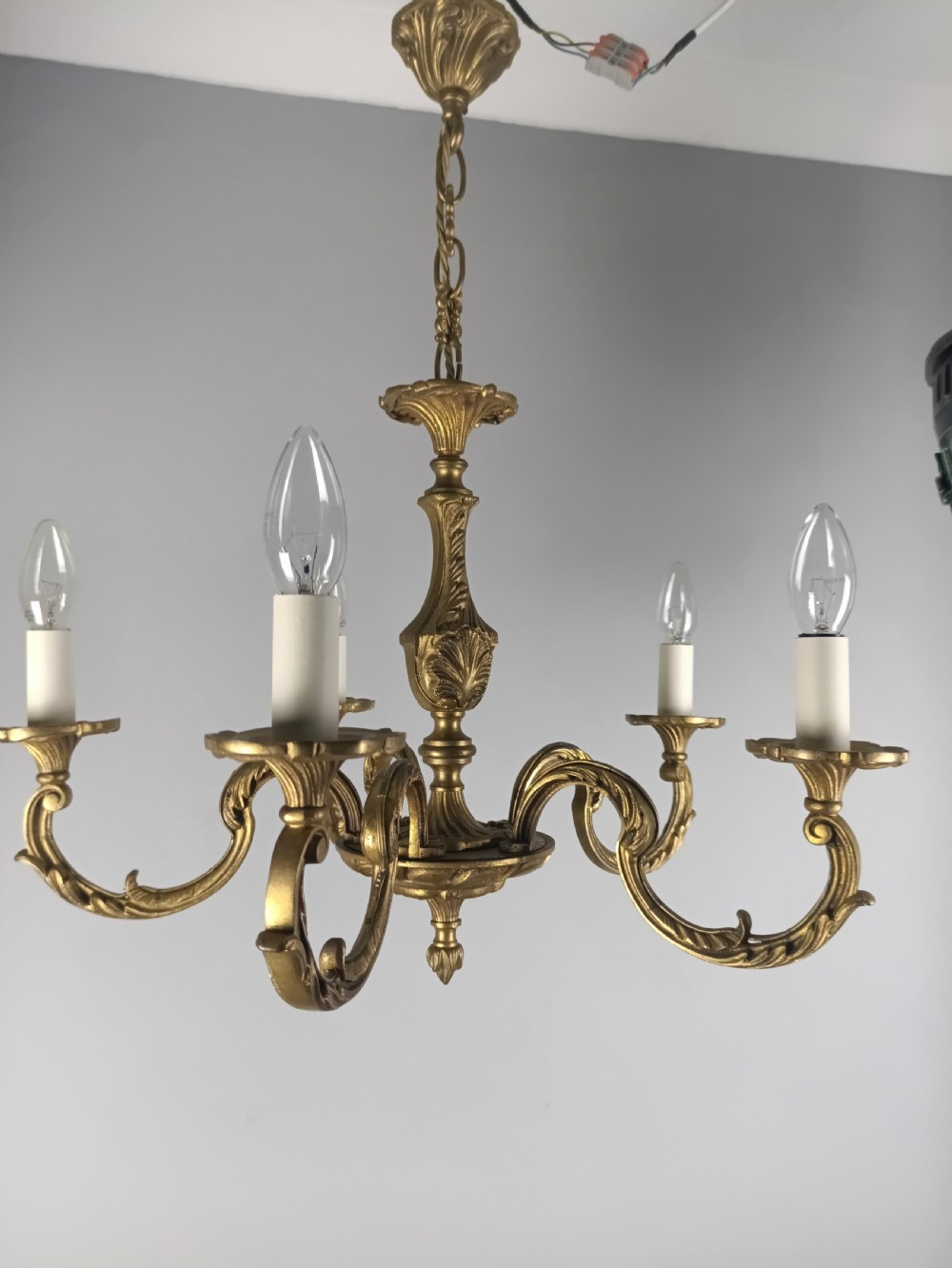 A French gilt brass five-arm chandelier featuring ornate scrolled branches, leaf motifs, and candle bulb sockets suspended from a central chain. View IV