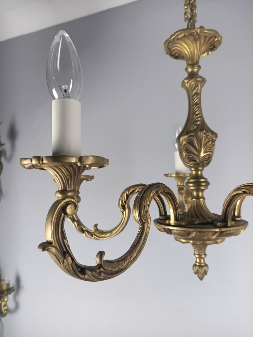A French gilt brass five-arm chandelier featuring ornate scrolled branches, leaf motifs, and candle bulb sockets suspended from a central chain. View VII