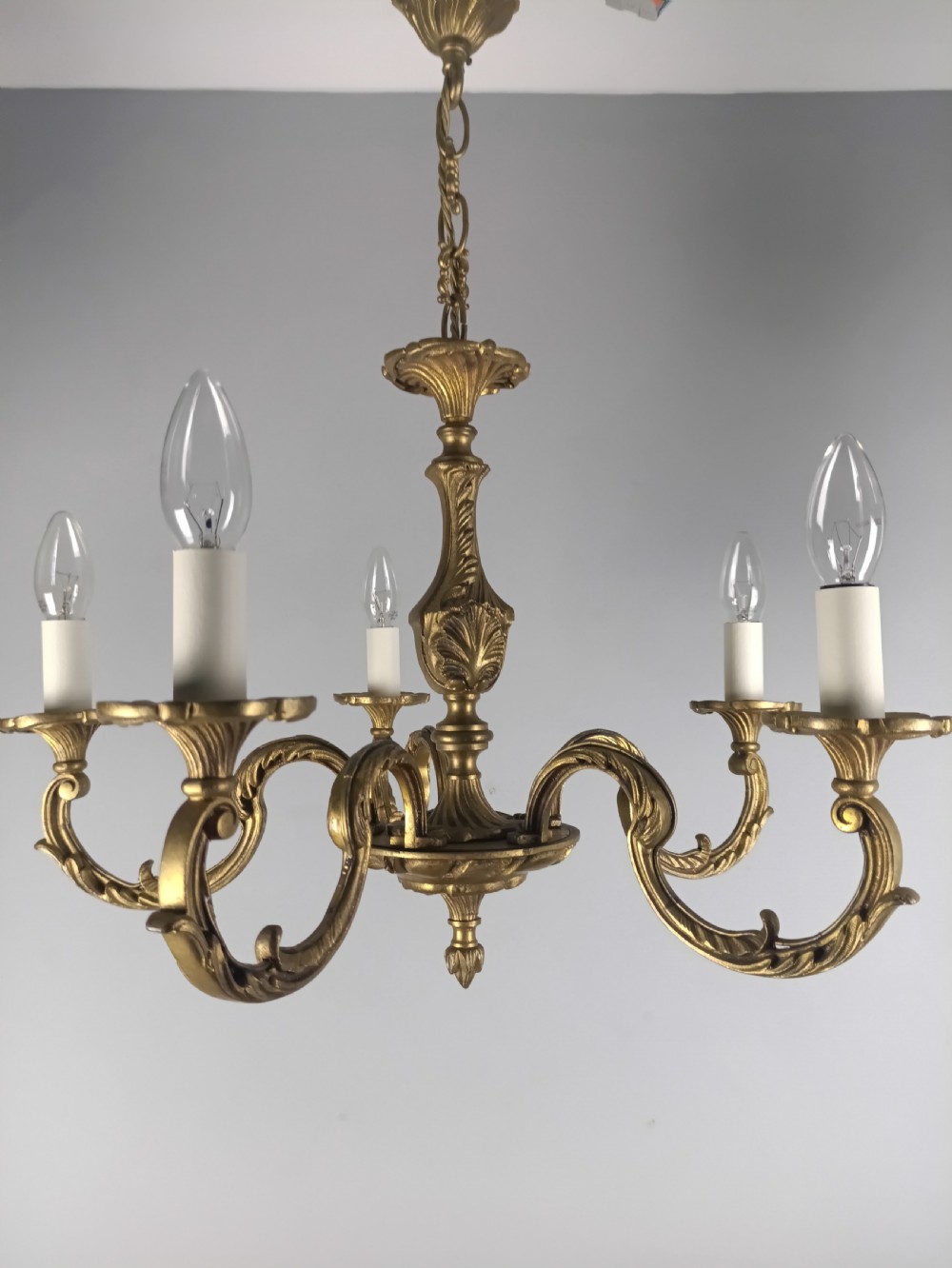 A French gilt brass five-arm chandelier featuring ornate scrolled branches, leaf motifs, and candle bulb sockets suspended from a central chain. View VIII