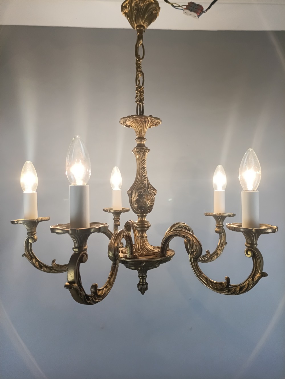 A French gilt brass five-arm chandelier featuring ornate scrolled branches, leaf motifs, and candle bulb sockets suspended from a central chain. View IX