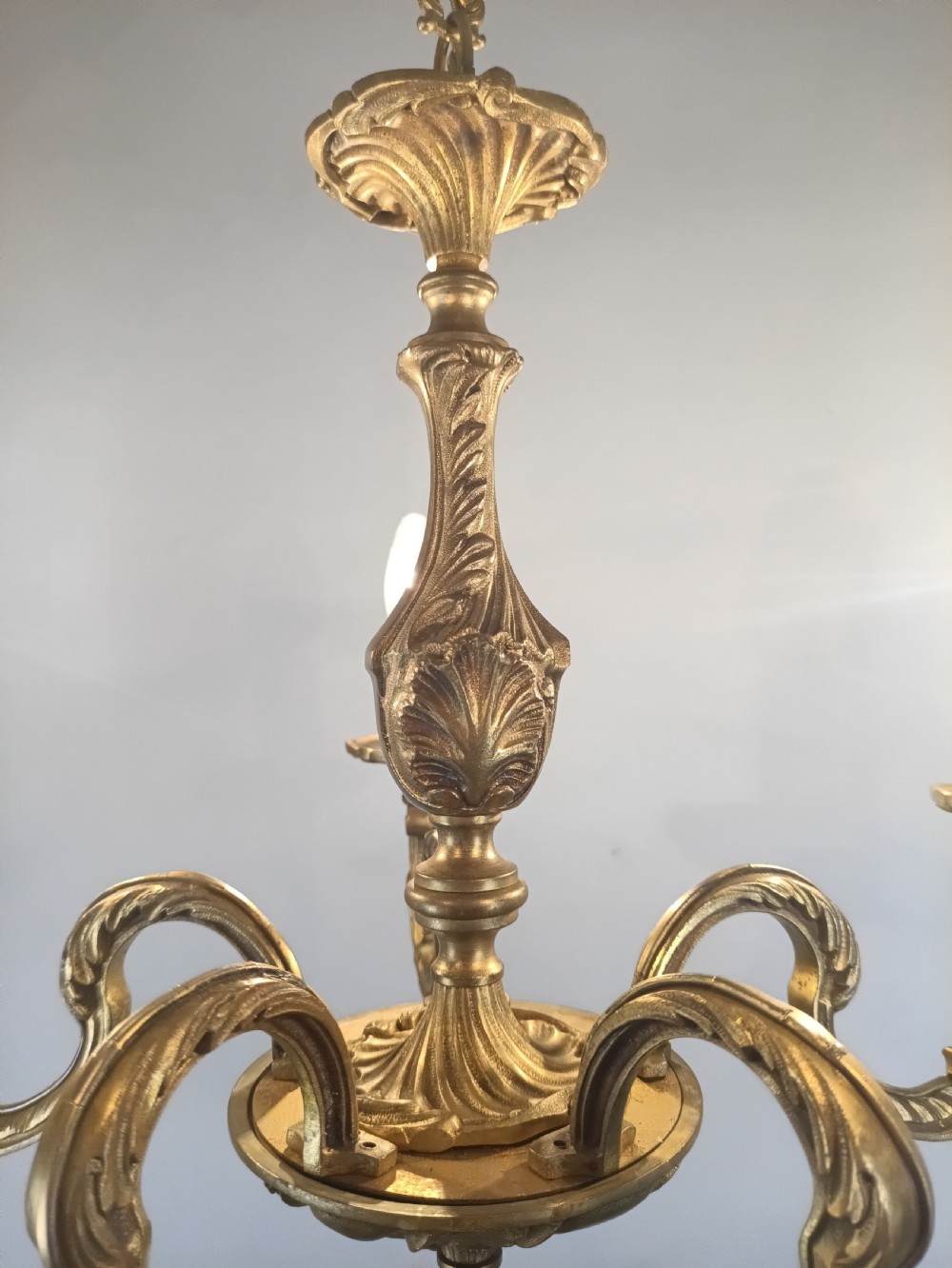 A French gilt brass five-arm chandelier featuring ornate scrolled branches, leaf motifs, and candle bulb sockets suspended from a central chain. View X