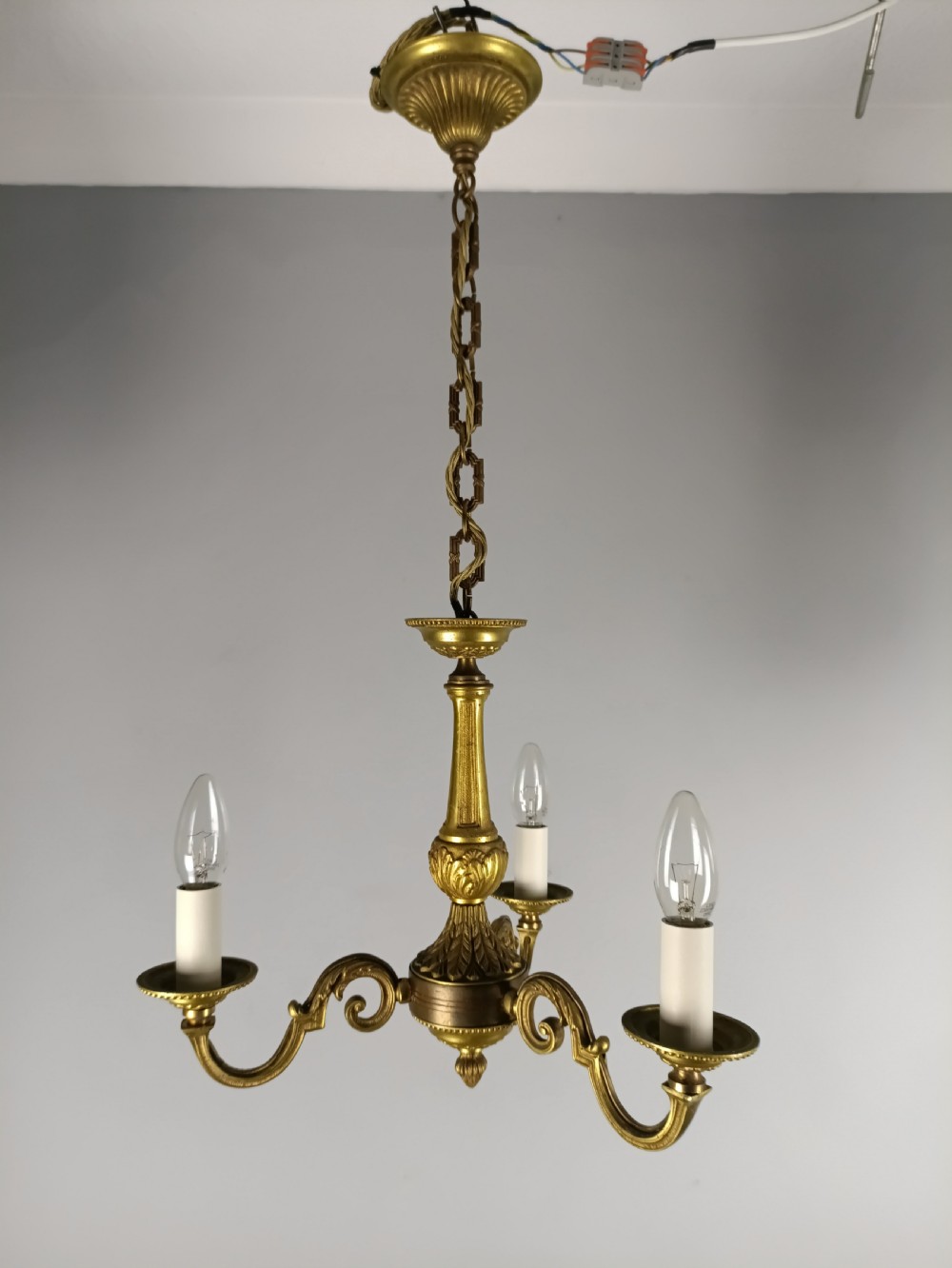 A three-arm gilt brass ceiling chandelier featuring scrolled branches, acanthus leaf decoration, and a central tapered column suspended by a chain. View III