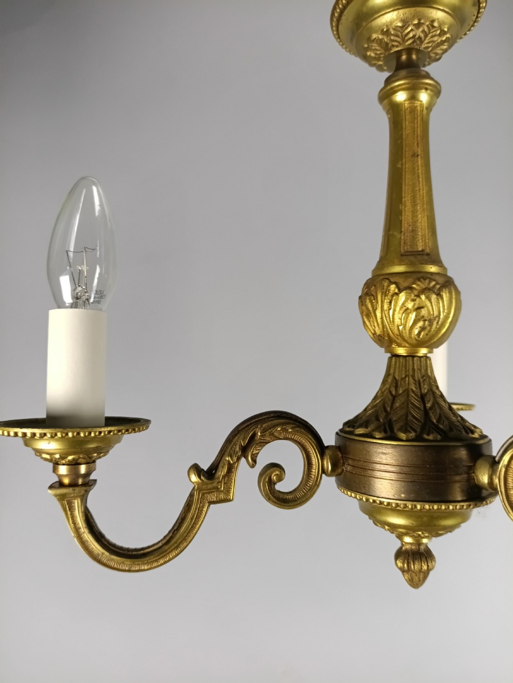 A three-arm gilt brass ceiling chandelier featuring scrolled branches, acanthus leaf decoration, and a central tapered column suspended by a chain. View VI