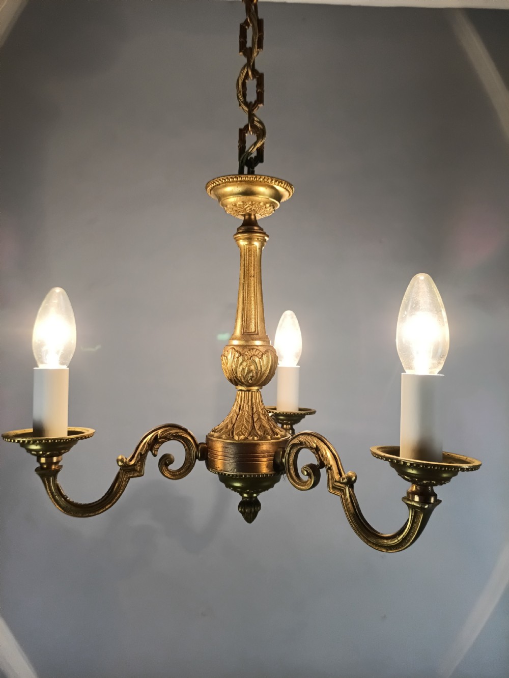 A three-arm gilt brass ceiling chandelier featuring scrolled branches, acanthus leaf decoration, and a central tapered column suspended by a chain. View XI