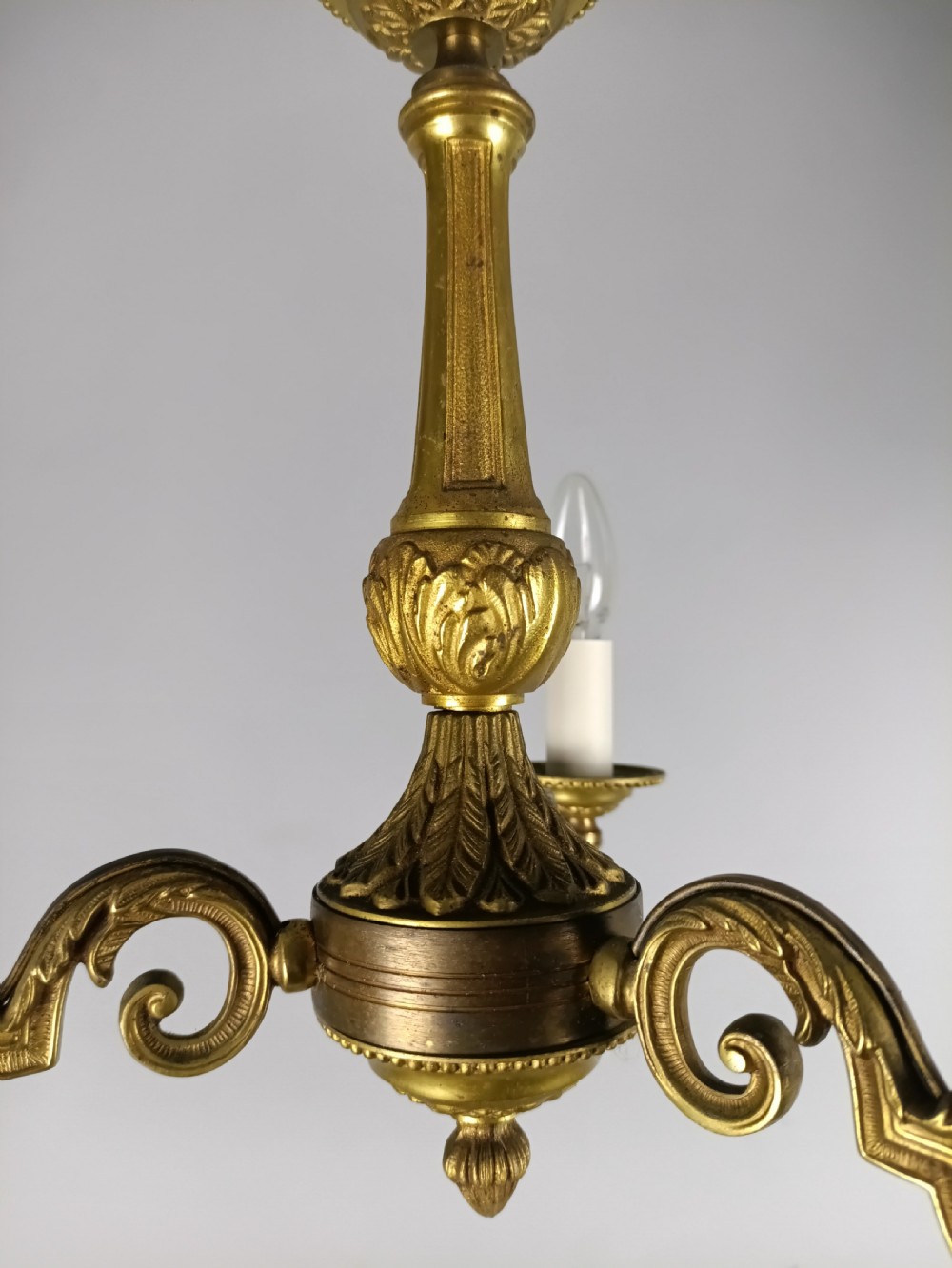 A three-arm gilt brass ceiling chandelier featuring scrolled branches, acanthus leaf decoration, and a central tapered column suspended by a chain. View XV