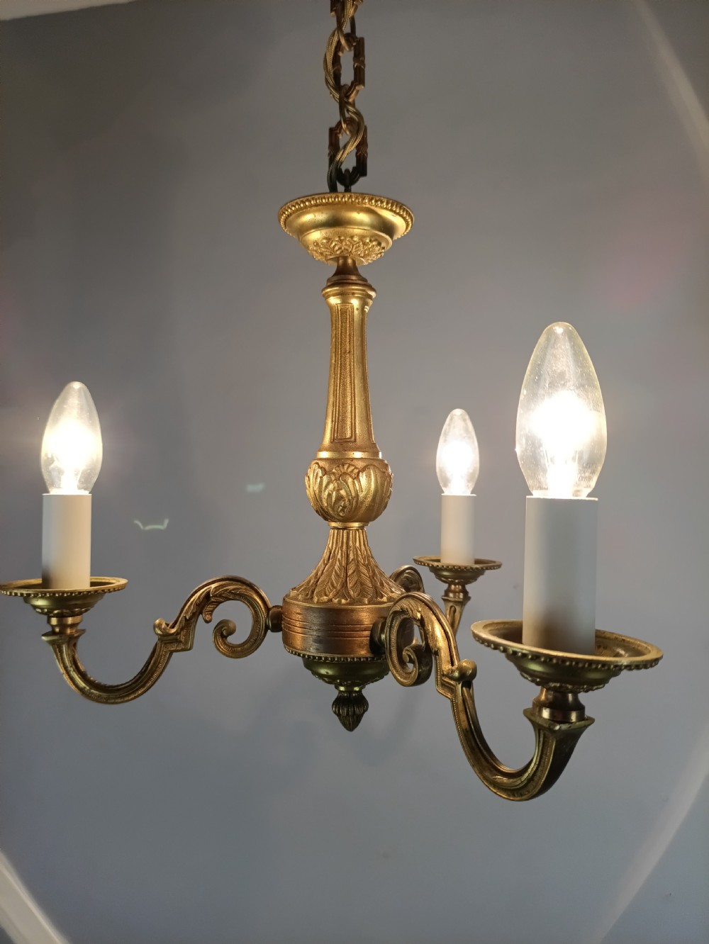 A three-arm gilt brass ceiling chandelier featuring scrolled branches, acanthus leaf decoration, and a central tapered column suspended by a chain. View XIX