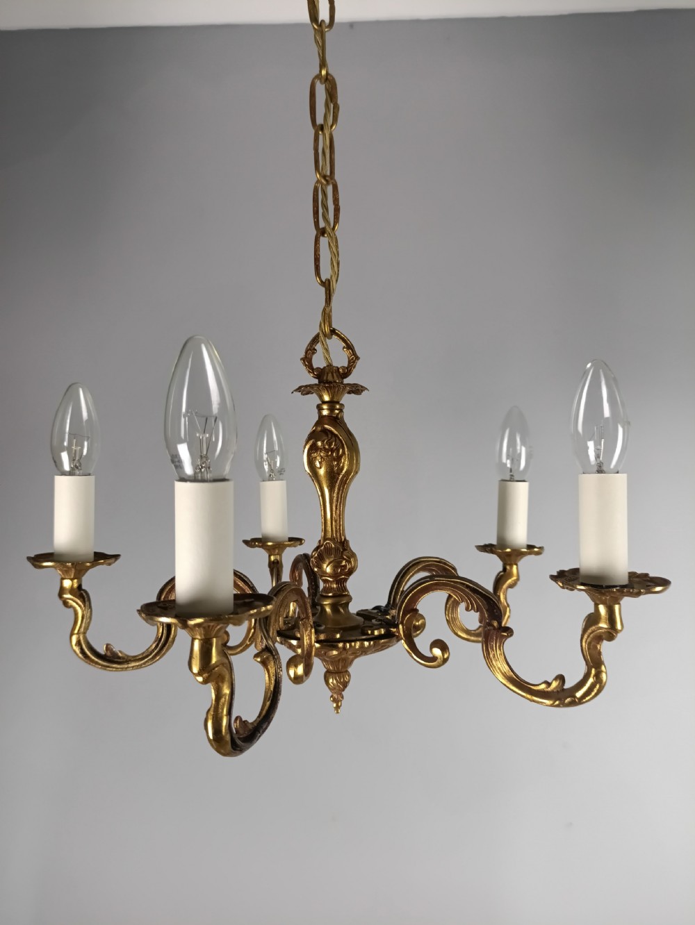 A French five-light gilt bronze chandelier featuring scrolling Rococo arms, candle-style bulb holders, and a central chased stem.
