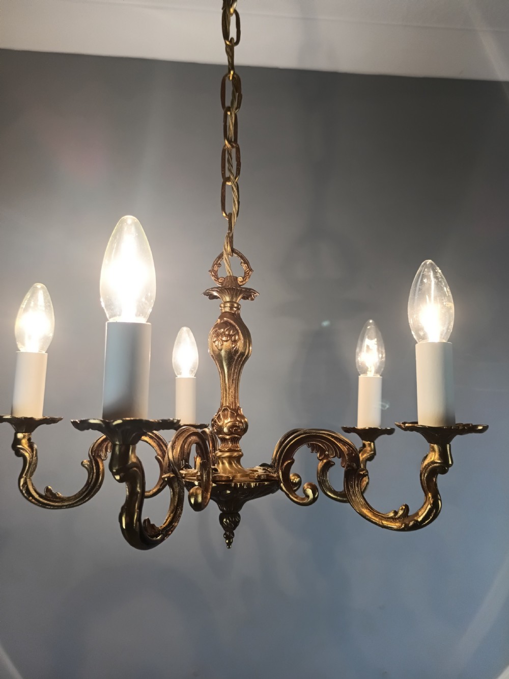 A French five-light gilt bronze chandelier featuring scrolling Rococo arms, candle-style bulb holders, and a central chased stem. View IX